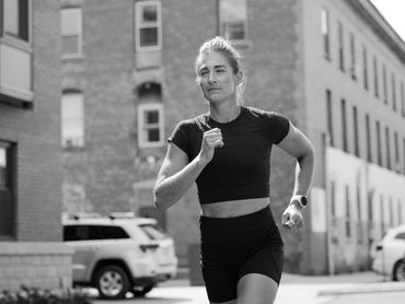 A woman jogging outdoors in athletic wear with a focused expression.