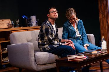 Two people sitting on a couch, one comforting the other, in a dimly lit room.