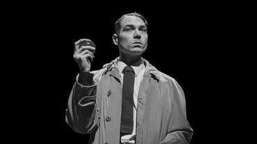 Man in trench coat holding an apple, staring intently.