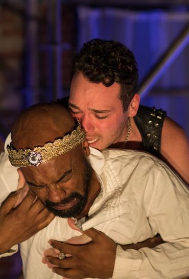 Two men in an emotional embrace, one wearing a crown and white shirt.