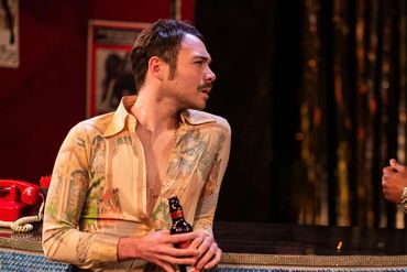 Two men engaged in conversation at a bar with expressive body language.