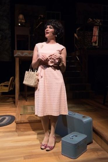 Woman in vintage dress with suitcases on stage during a theatrical performance.