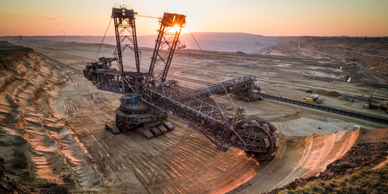 A large bucket-wheel excavator at a mining site during sunset.