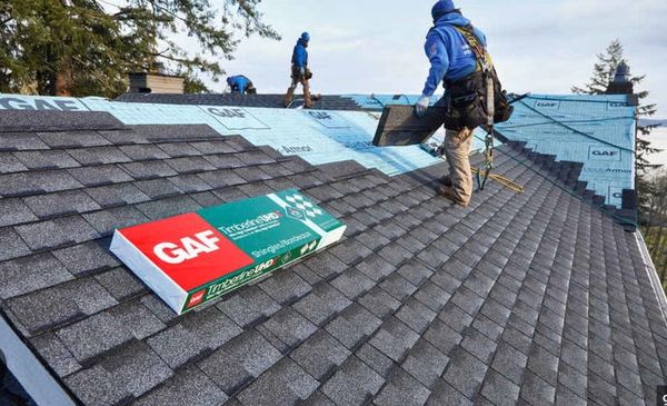 Workers installing GAF Timberline HD shingles on a roof under sunny weather.