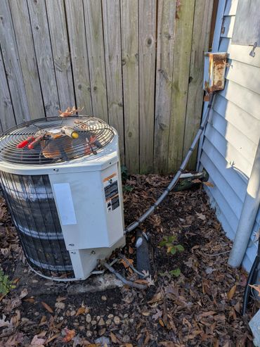 Outdoor air conditioning unit with tools on top beside a wooden fence.