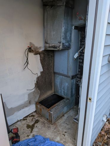 Old rusty metal furnace vent with exposed wiring and stains on the wall.