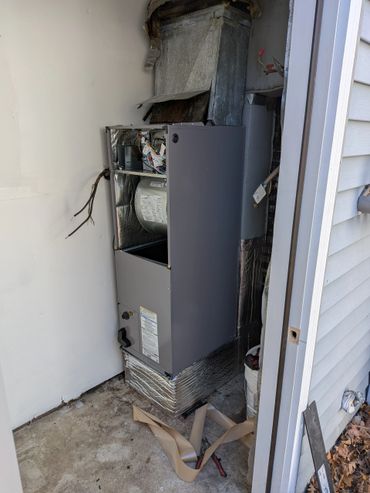 Installation of a partially assembled HVAC unit in an outdoor utility closet.