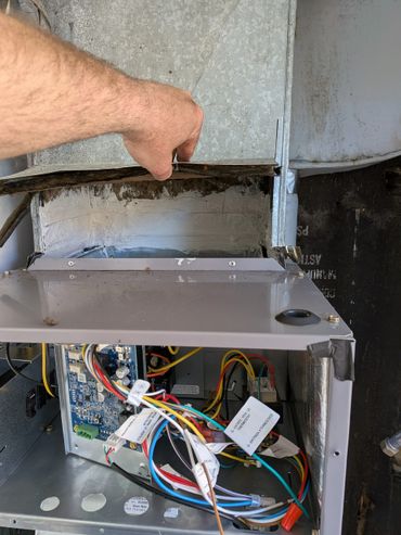 Hand lifting metal panel to reveal wires inside HVAC unit.