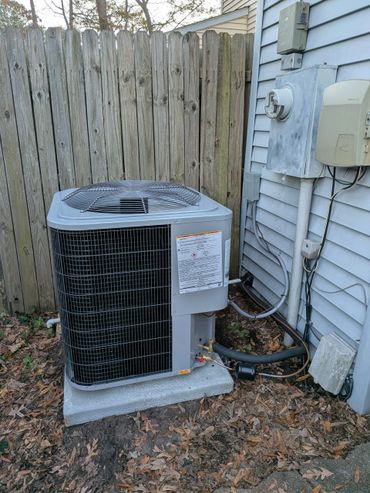 Outdoor air conditioning unit installed beside a house and wooden fence.