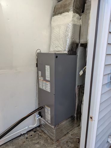 Modern HVAC unit installed in a small outdoor space with insulated ductwork.