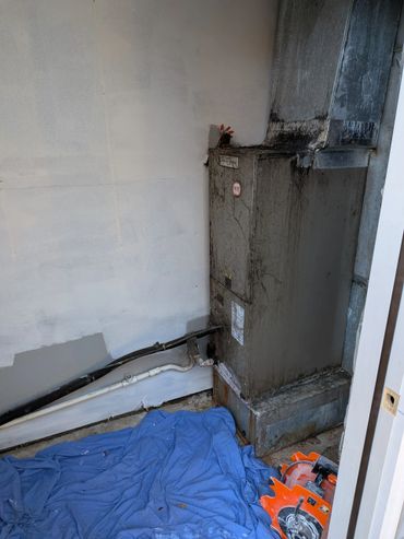 Old dirty HVAC unit with pipes and blue tarp on the floor.