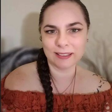 Woman with braided hair wearing an off-shoulder red top smiles at the camera.