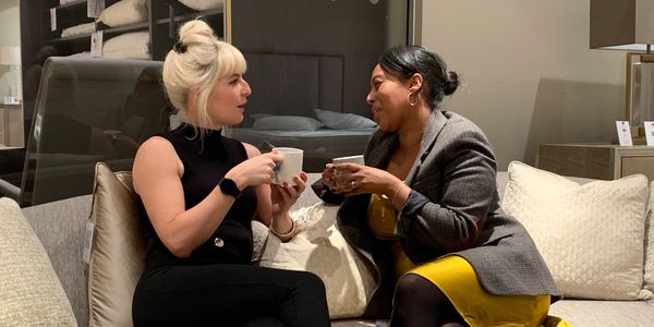 Two women chatting and drinking coffee on a couch in a cozy setting.