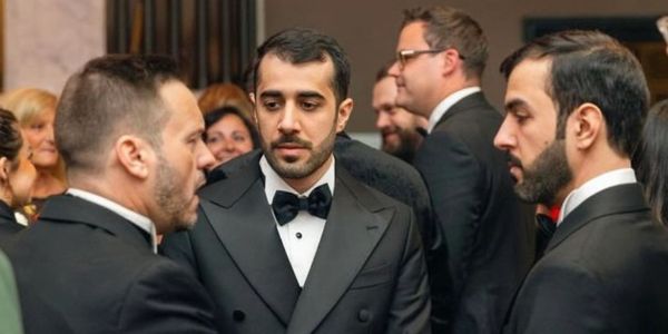 Three men in tuxedos engaged in conversation at a formal event.