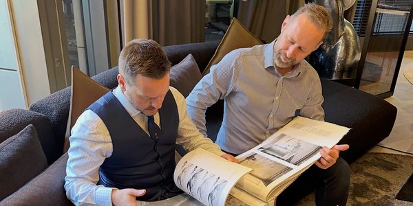 Two men in formal attire reviewing documents on a couch in a modern office.