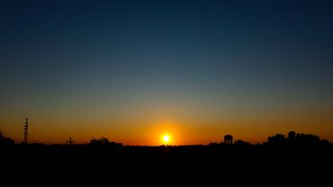 Sun setting behind a silhouetted cityscape with a gradient sky.