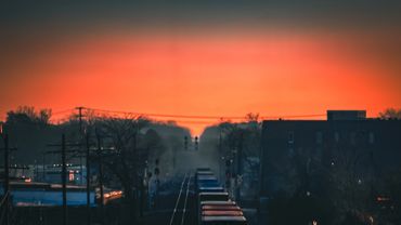 A freight train moves through a town at sunset with a vibrant orange sky.
