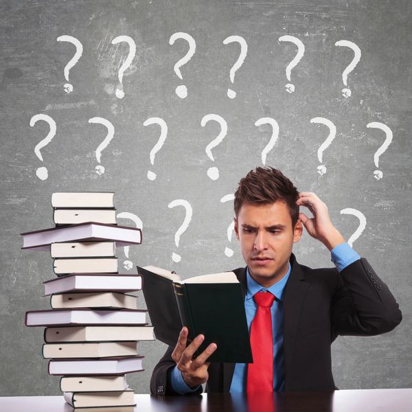 MAN WEARING A SUIT SCRATCHING HIS HEAD WITH A PILE OF BOOKS AND QUESTIONMARKS ABOVE HIS HEAD