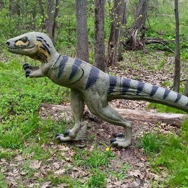 A life-sized dinosaur model in a forested area.