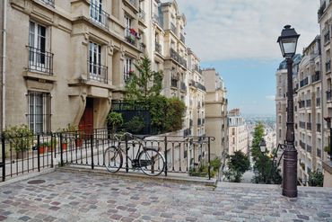 A bicycle parked by a railing on a cobblestone street in a historic European city.