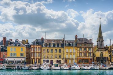 Colorful historic buildings and boats line a waterfront under a cloudy sky.