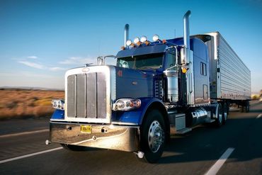 Blue semi-truck driving on an open highway under a clear sky.