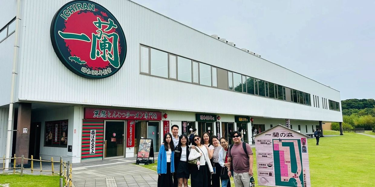 Group of people posing outside Ichiran ramen restaurant with a large sign.