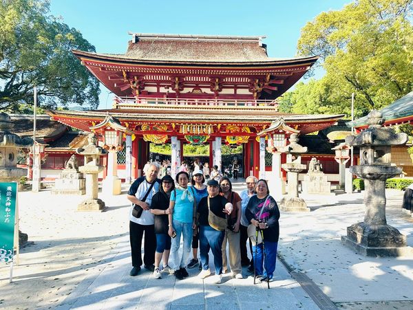 A group of tourists posing in front of a traditional Japanese shrine gate.