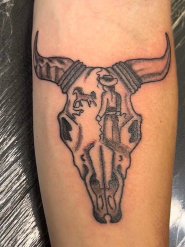 Tattoo of a bull skull with a cowboy and horse inside it on a forearm.