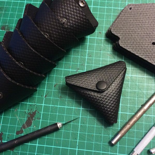Black textured leather cases and crafting tools on a green cutting mat.