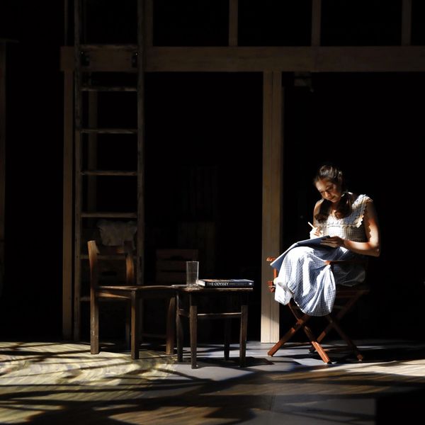 Woman writing in a notebook under a spotlight.