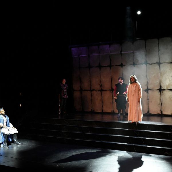 Theatrical stage with actors in costume under dramatic lighting.
