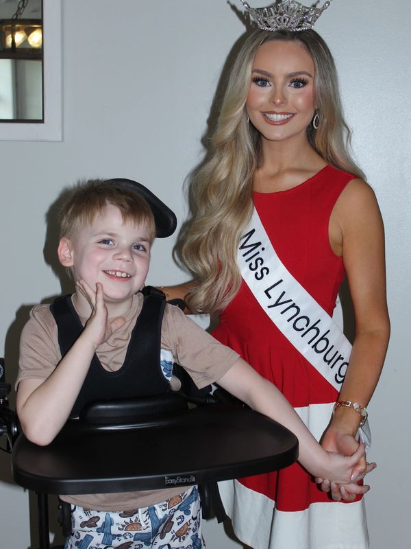 Miss Lynchburg smiling and holding hands with a young boy in a wheelchair.