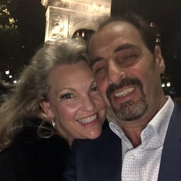 Smiling couple taking a selfie at night near an illuminated arch.