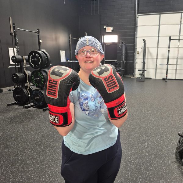 Person wearing boxing gloves posing in a gym.