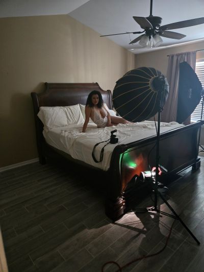 Woman posing on a bed during a photoshoot in a dimly lit room.