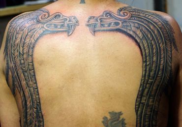 Black and grey tattoo of a pair of Aztec dragons on a man's back.
