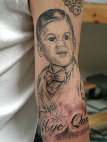 Black and grey portrait tattoo of a young child with lettering on an arm.