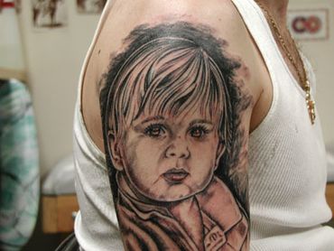 Black and grey portrait tattoo of a young child on an arm.