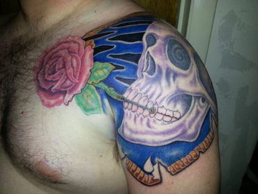 Black and grey tattoo skull with a red rose on a blue background.
