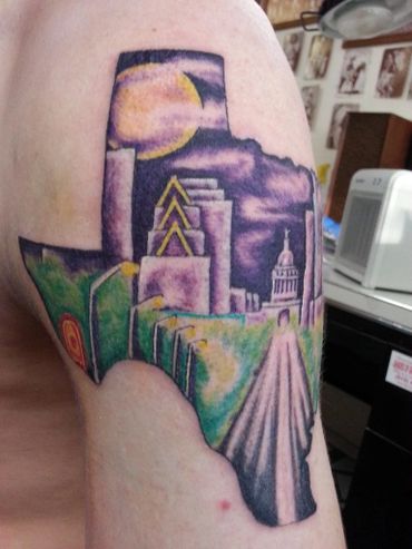 Color tattoo of an outline of Texas with the scene of the road to the capitol on the inside.