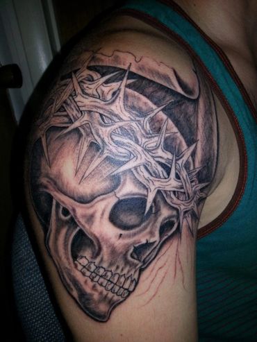 Thorn of crowns on a black and grey tattoo skull on a shoulder.