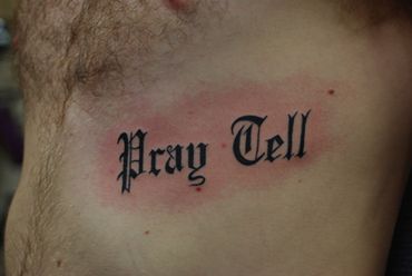 Old English in black lettering tattoo on man's torso.