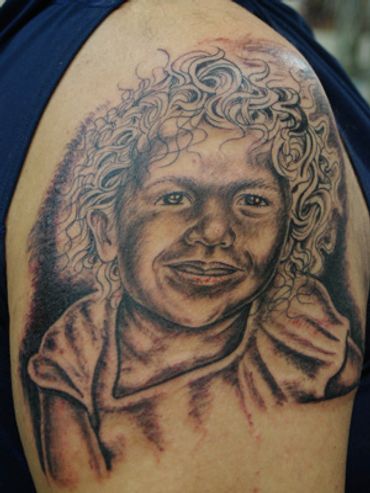 Black and grey portrait tattoo of child on a shoulder.