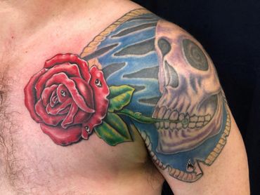 Color red rose with a skull tattoo on a man's shoulder.
