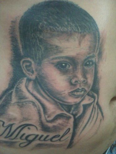 Black and grey portrait tattoo of a young boy with lettering.
