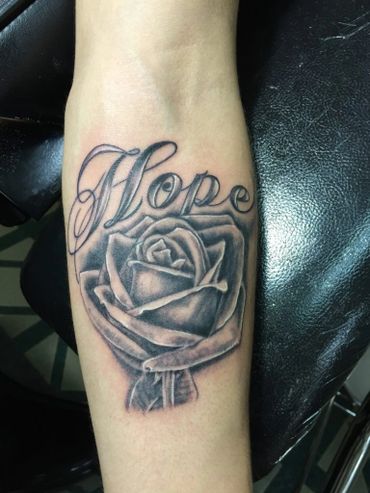Black and grey rose tattoo with a name on inner lower arm.