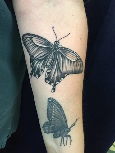 Two black and grey butterfly tattoos on an arm.