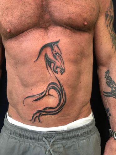 Black and grey stylized horse head tattoo on a man's torso.