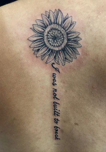 Black and gey sunflower with script lettering on a woman's back.
